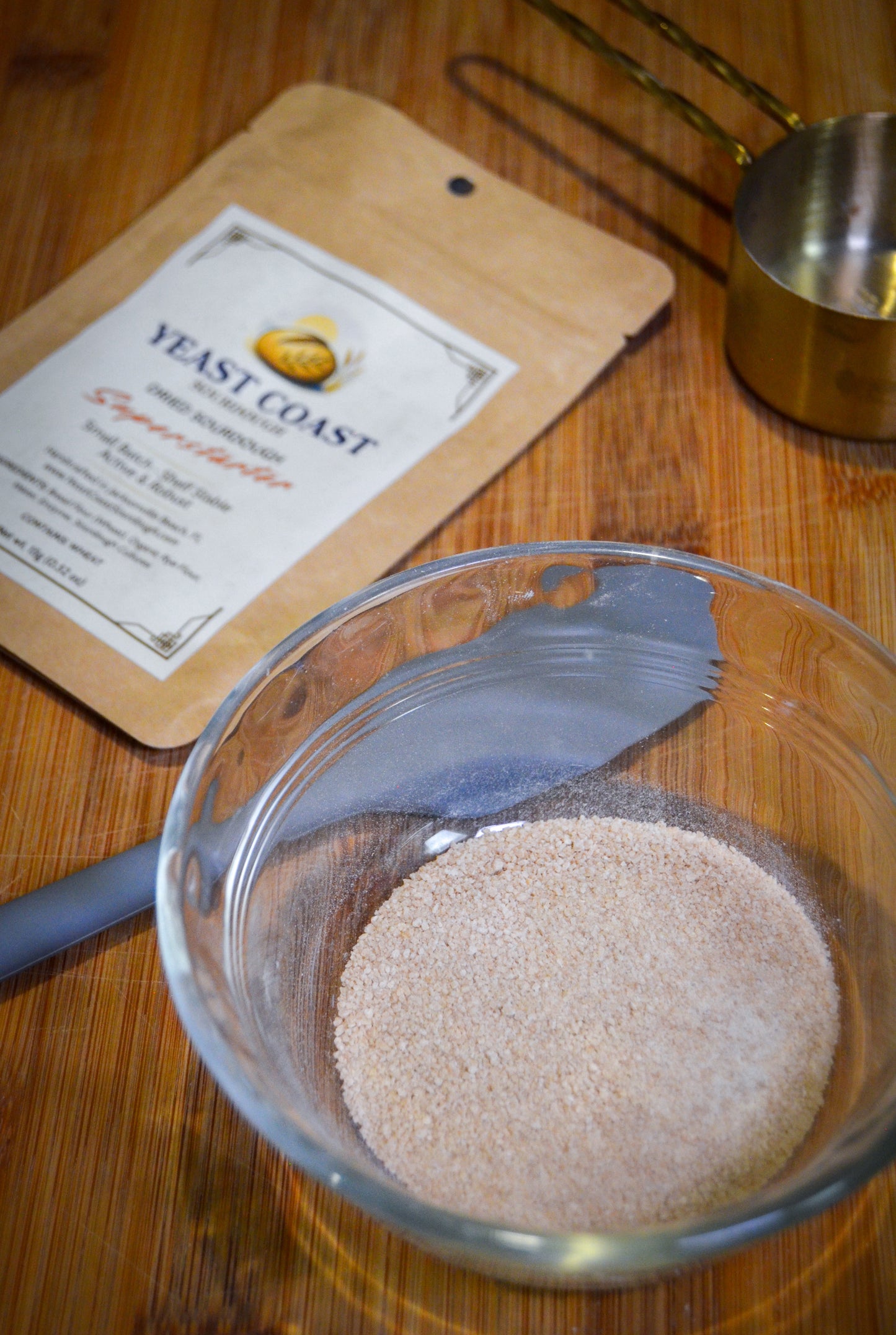 Glass bowl with sourdough starter and a measuring spoon on a wooden surface