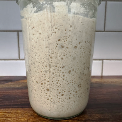 Glass jar with a fermented dough starter on a wooden surface and tiled wall background