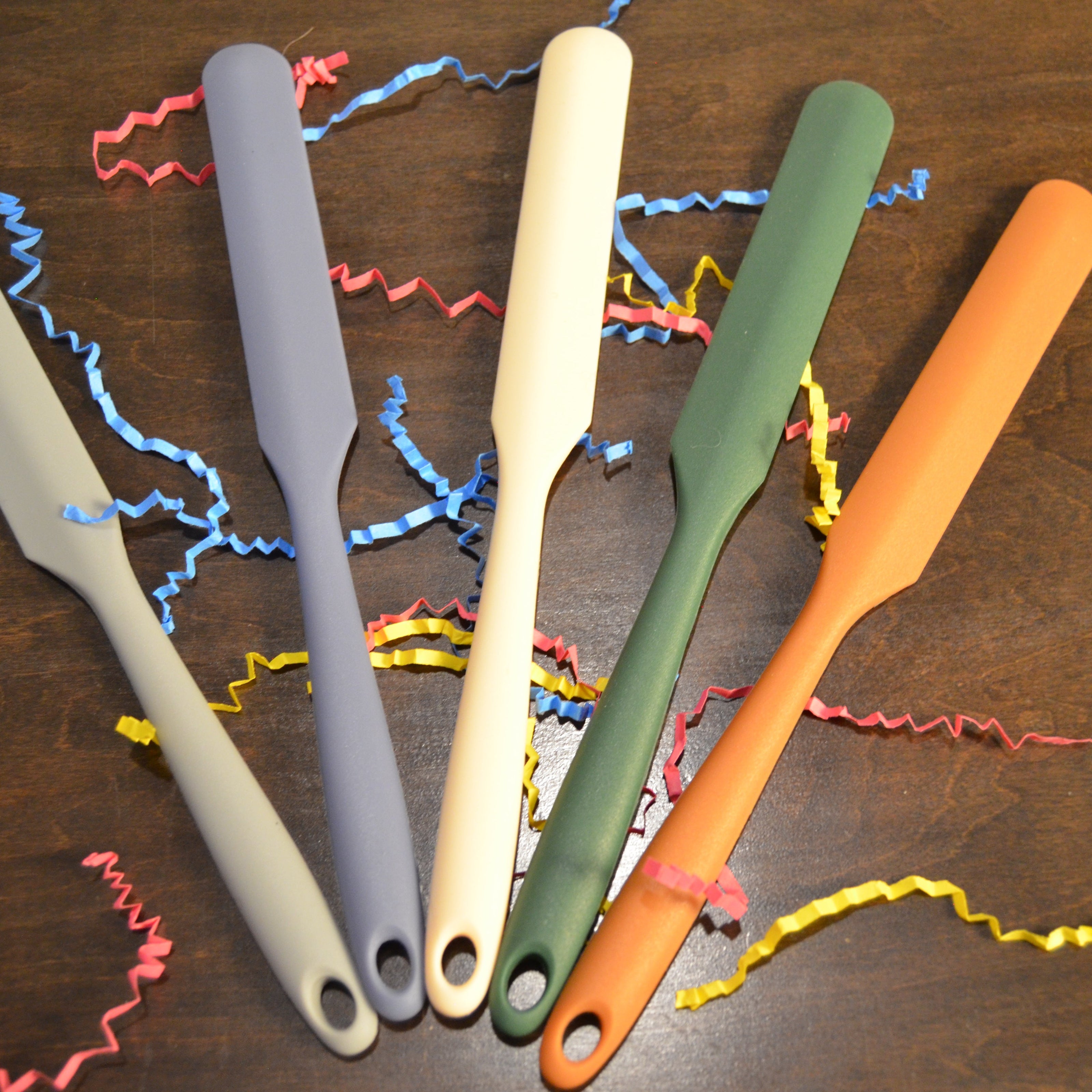 Five colorful spatulas on a wooden surface with colorful ribbons.